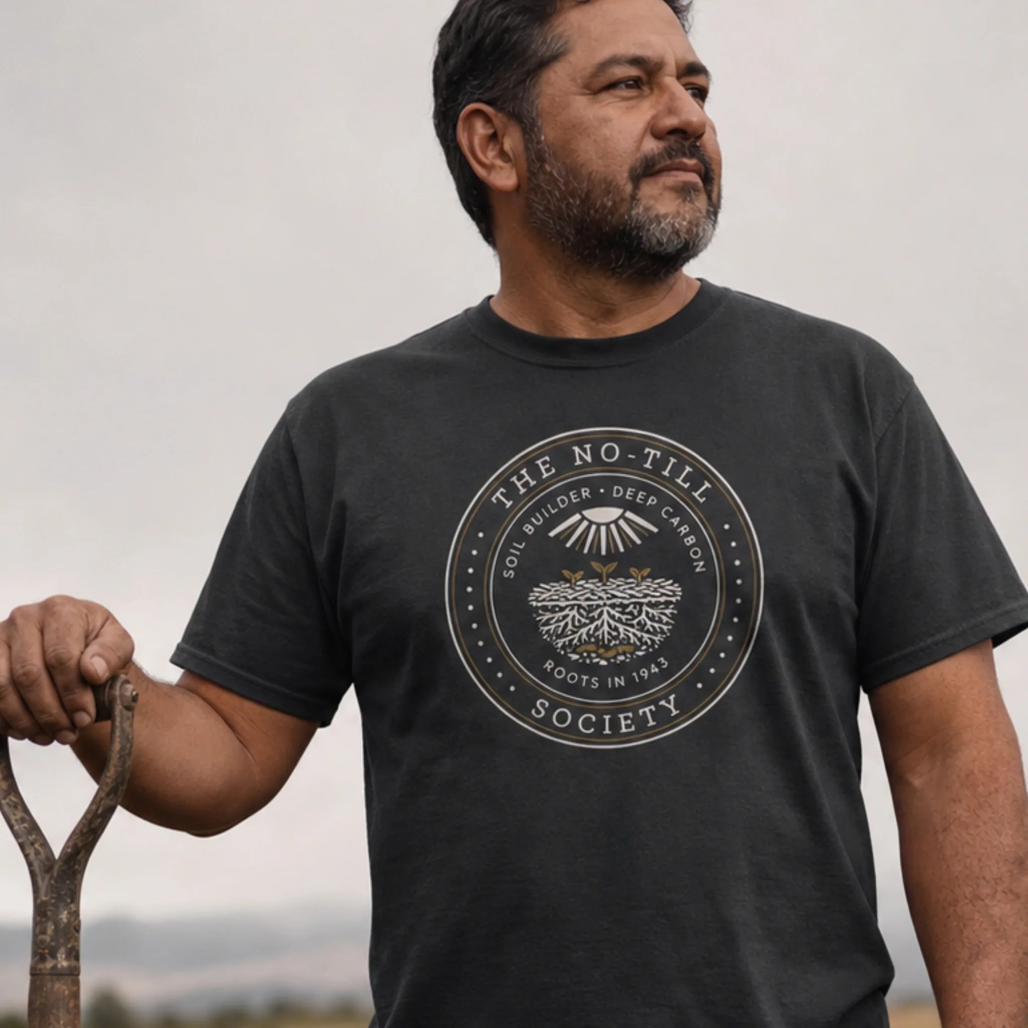 No-Till Society organic cotton t-shirt worn by man overlooking regenerative farmland at sunset